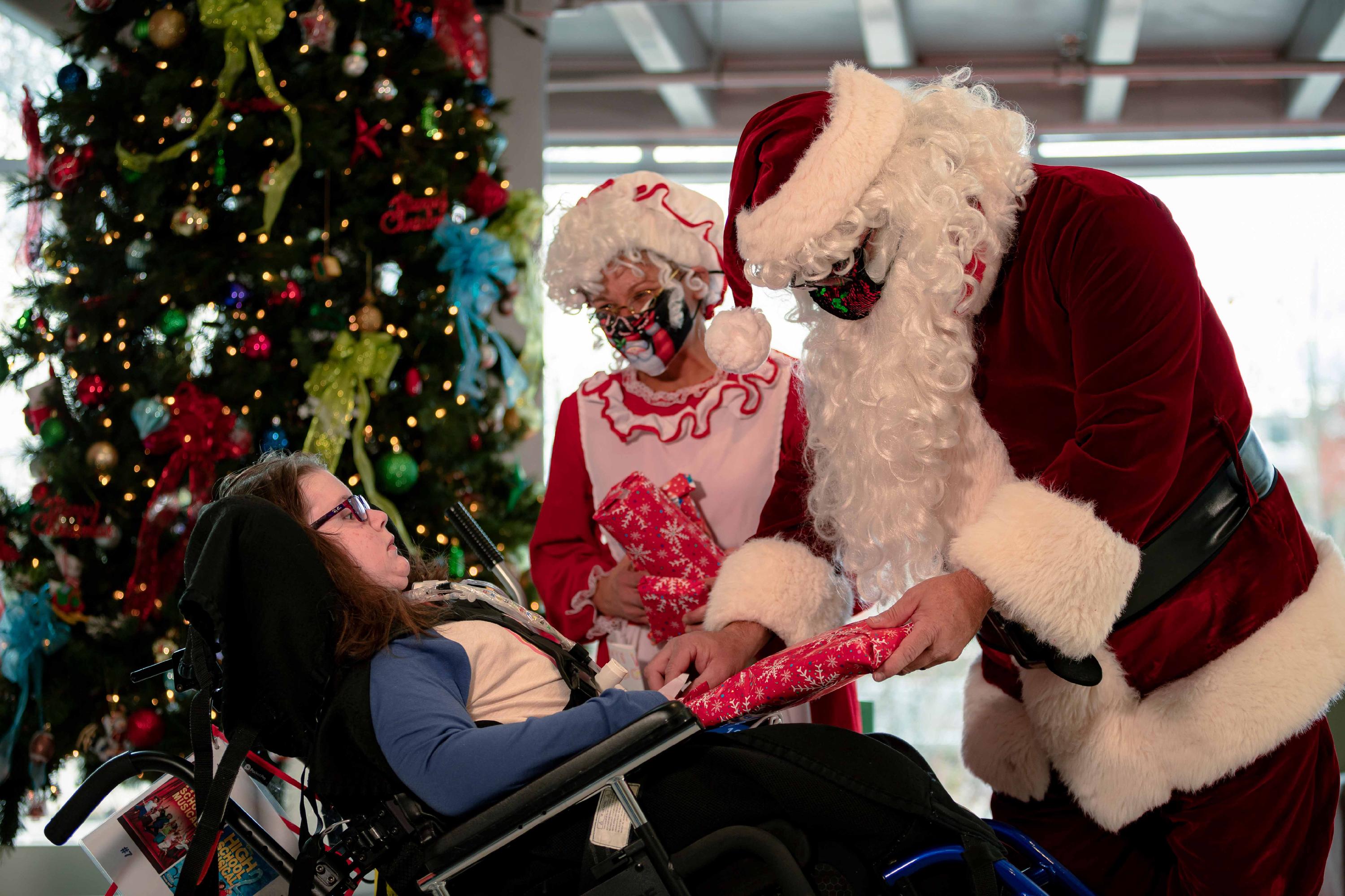 Santa and Mrs. Claus give a gift to a patient of Ranken Jordan Pediatric Bridge Hospital using a wheelchair